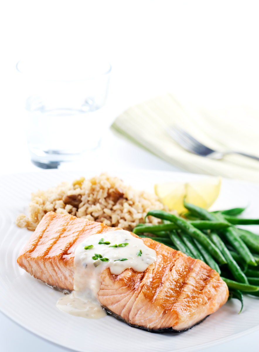 Dinner plate with salmon, green beans, rice, lemon, glass of water, and a fork on a napkin.