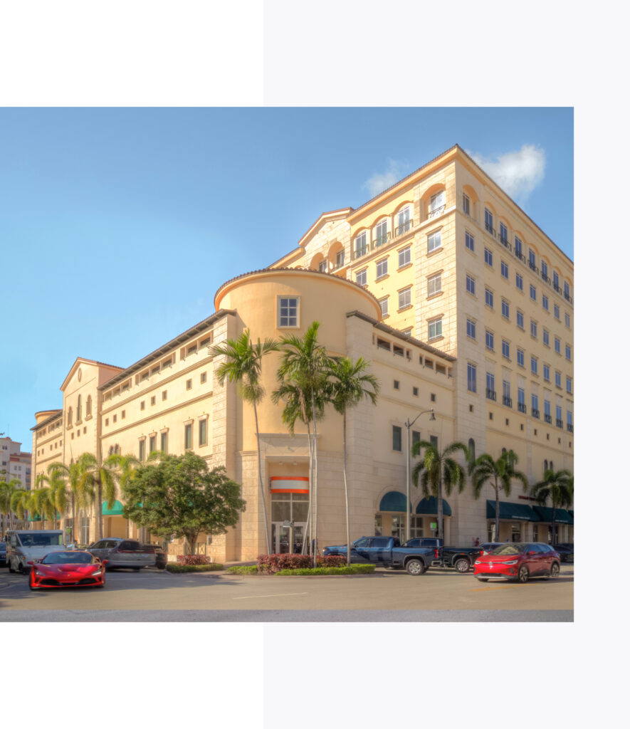 Street level view of 4000 Ponce Spanish Mediterranean exterior surrounded by cars and palm trees on a clear sunny day.